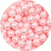 A close-up view of small, pink imitation pearl beads scattered on a white background.