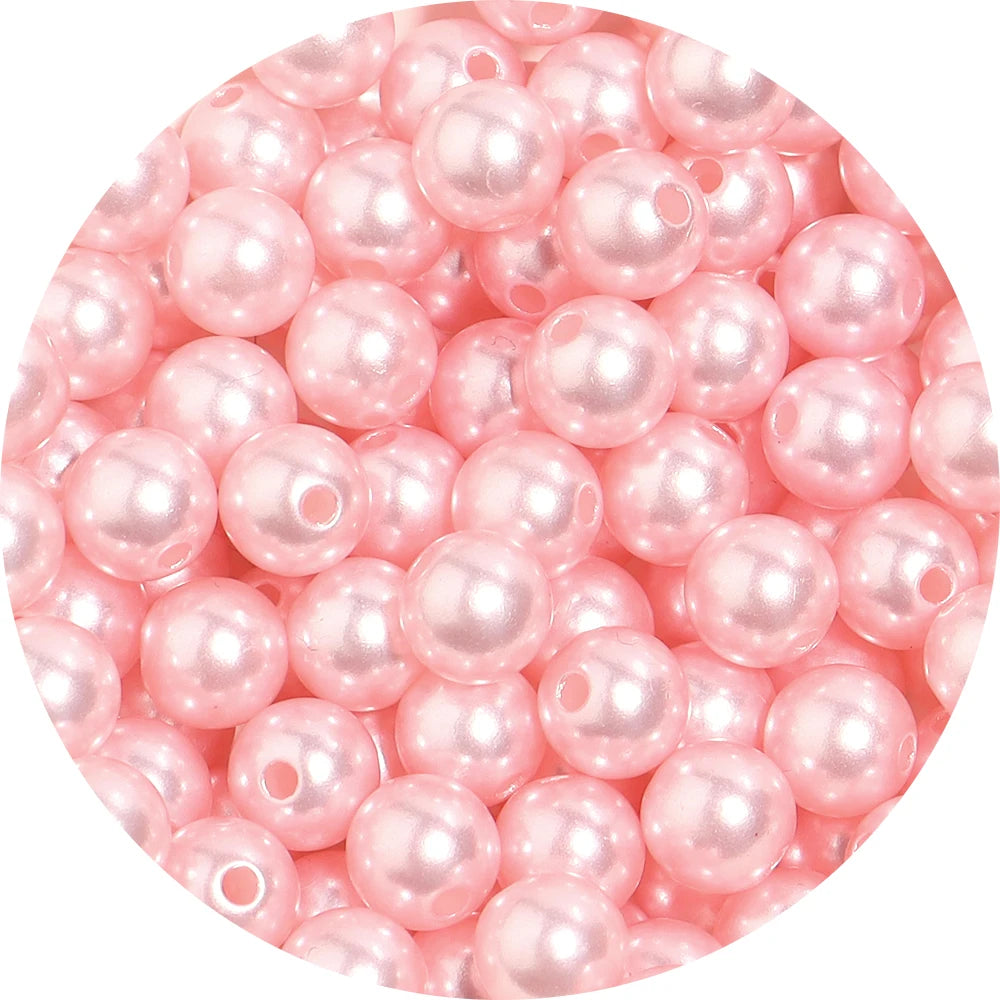 A close-up view of small, pink imitation pearl beads scattered on a white background.