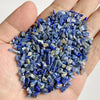 A hand holds a pile of deep blue and gray tumbled stone chips for jewelry making and home decor.