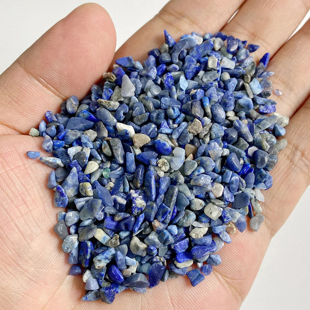 A hand holds a pile of deep blue and gray tumbled stone chips for jewelry making and home decor.