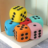 A collection of brightly colored jumbo soft foam dice in yellow, blue, red, orange, and pink resting on a white surface.