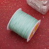 A spool of light mint green nylon knotting cord for jewelry making resting on a red glitter surface.