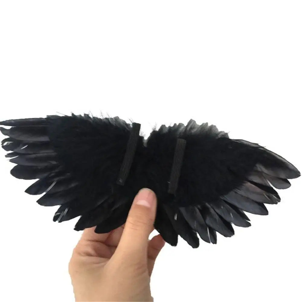 A hand holds a pair of black mini feather angel wings for dolls and crafts.