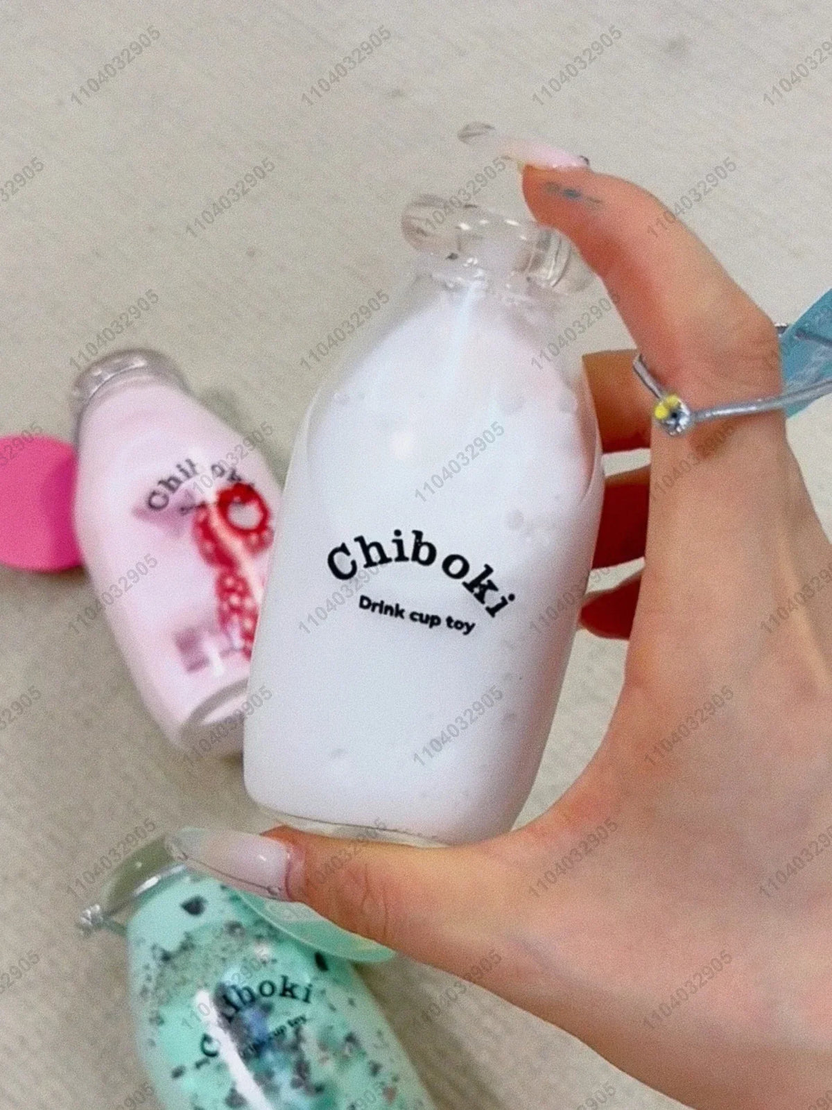 A hand holds a white bottle labeled Chiboki drink cup toy and a green squishy fidget toy.