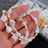 A hand holds a string of white pearl beads with gold accents and floral charms.