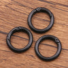 Three black metal O-ring spring clasps are arranged on a wooden surface.