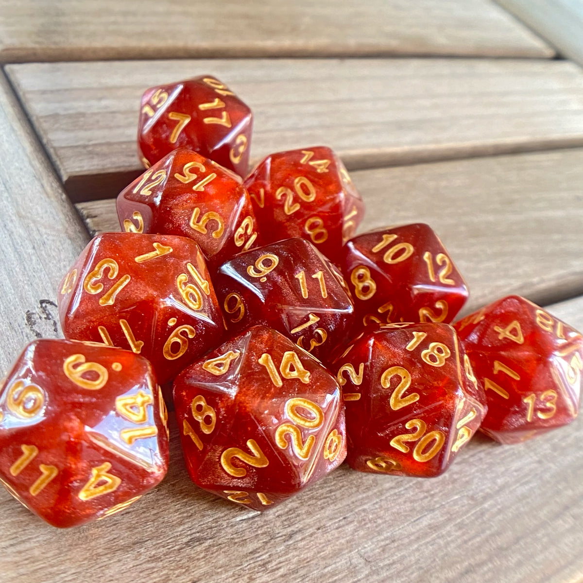 A collection of ten translucent red pearl acrylic D20 dice arranged on a wooden surface.