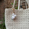 A light beige crocheted bag with a small white rabbit keychain hanging from the strap.