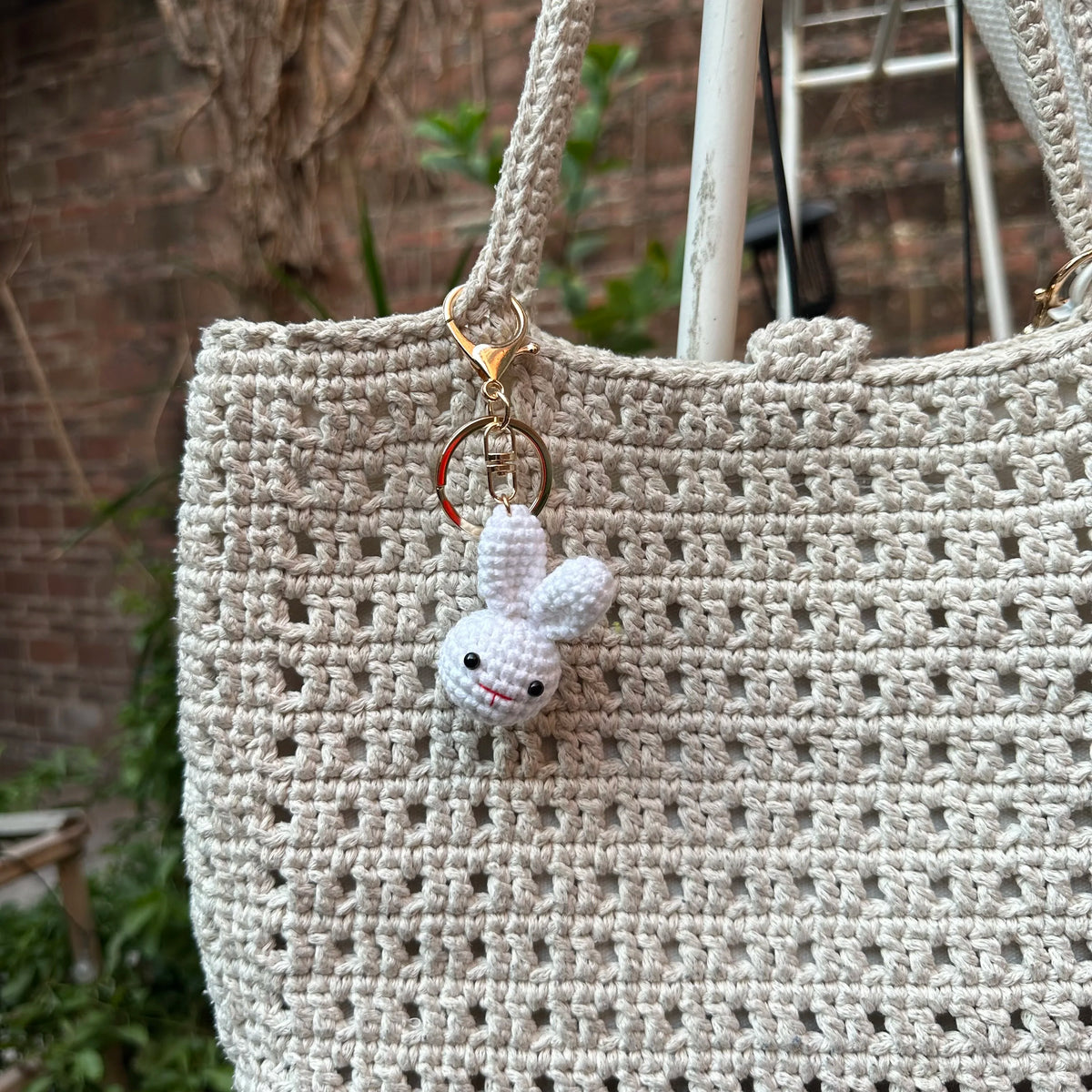 A light beige crocheted bag with a small white rabbit keychain hanging from the strap.