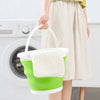 A hand holds a lime green collapsible bucket with a white lid, positioned above a white washing machine.