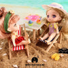 A miniature doll with pink hair and a floral hat is seated in a wooden chair on sand, next to a small pink ice cream cone.
