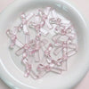 A collection of clear pink acrylic bow tie beads arranged on a white surface.