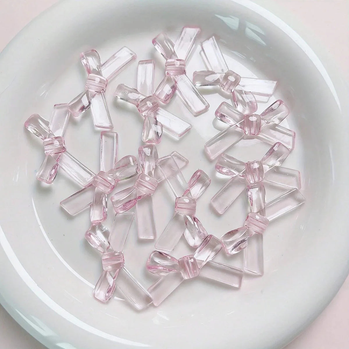 A collection of clear pink acrylic bow tie beads arranged on a white surface.