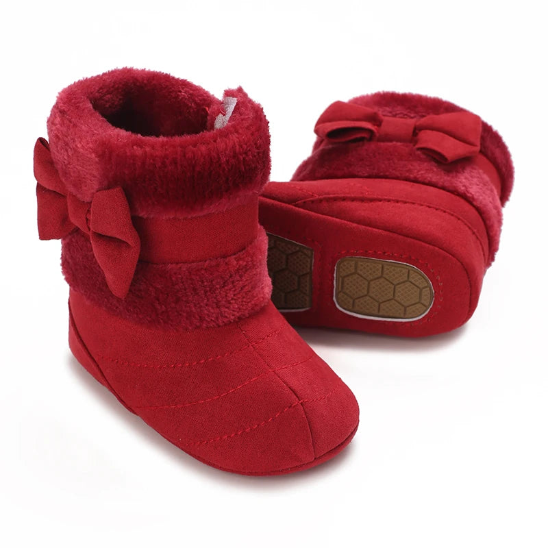 A pair of red faux fur baby first walker shoes with bow details.