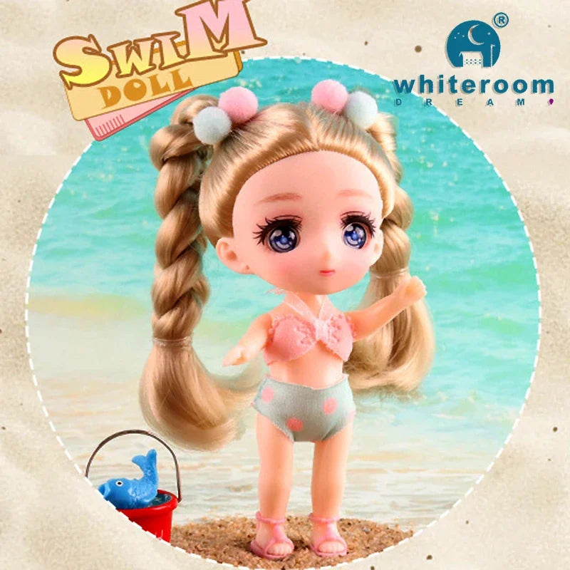 A pink doll with long blonde hair is shown standing on sand near the water, with a blue fish keychain nearby.