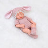 A realistic soft vinyl baby doll with a pink outfit and matching headband lying on white fur.