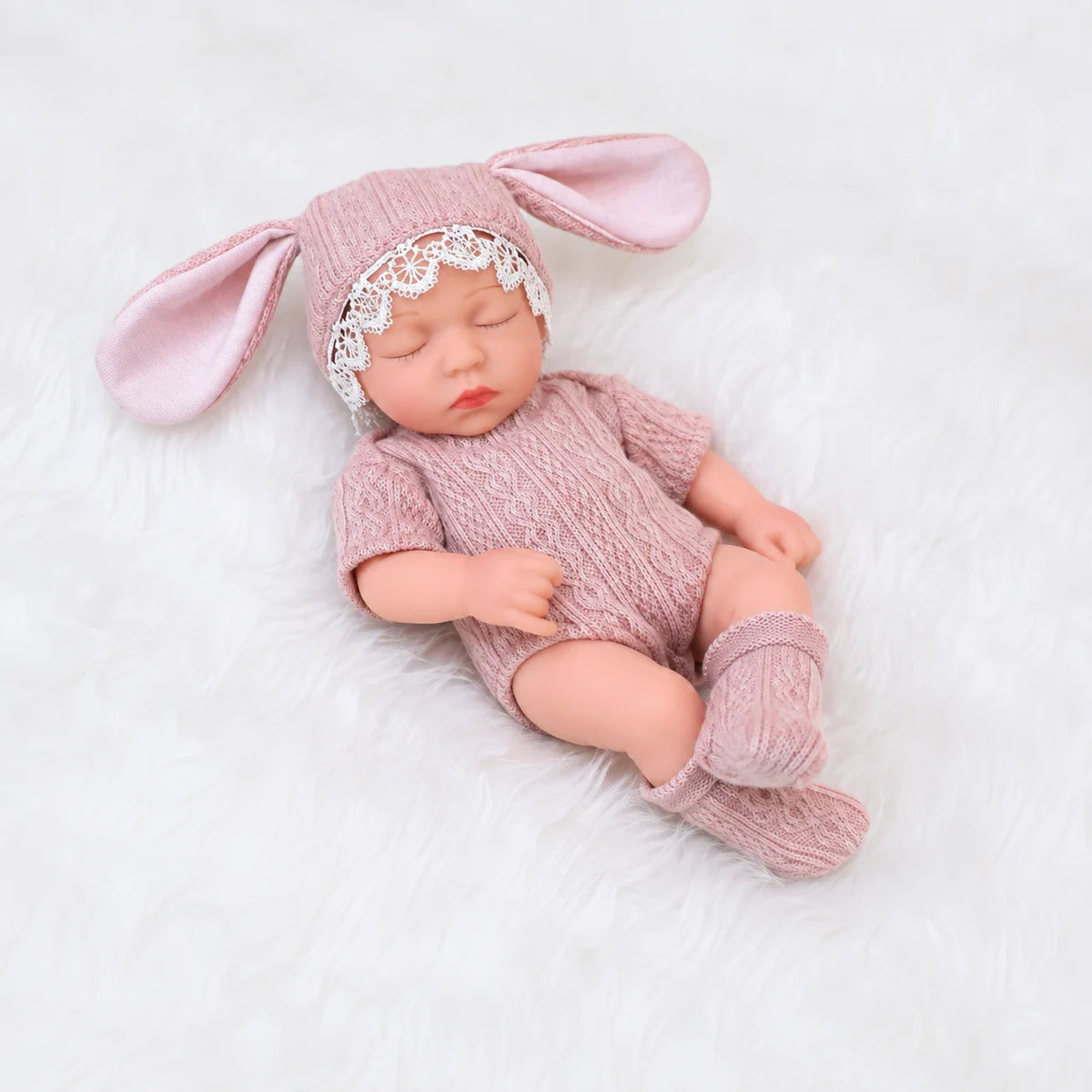A realistic soft vinyl baby doll with a pink outfit and matching headband lying on white fur.