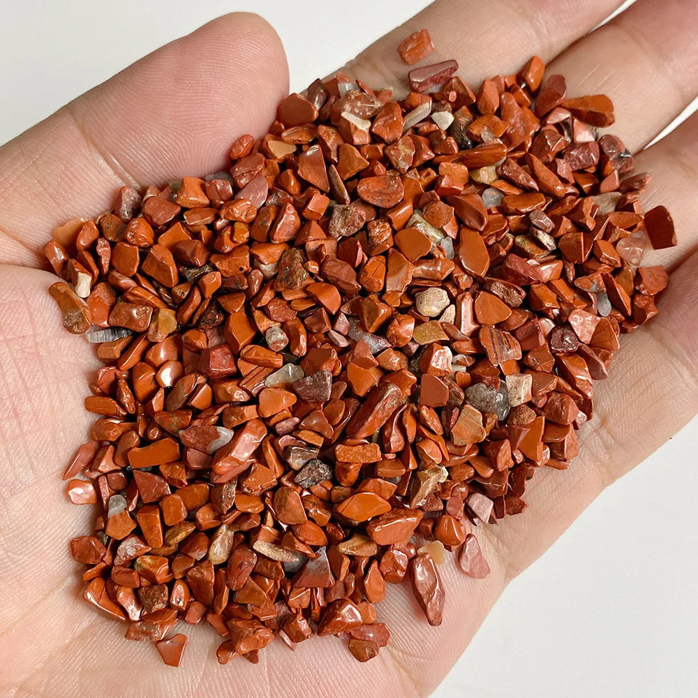 A hand holds a pile of reddish-brown tumbled stone chips for jewelry making and home decor.