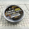 A tin of Camo Masking Putty for model painting placed on a grid background.
