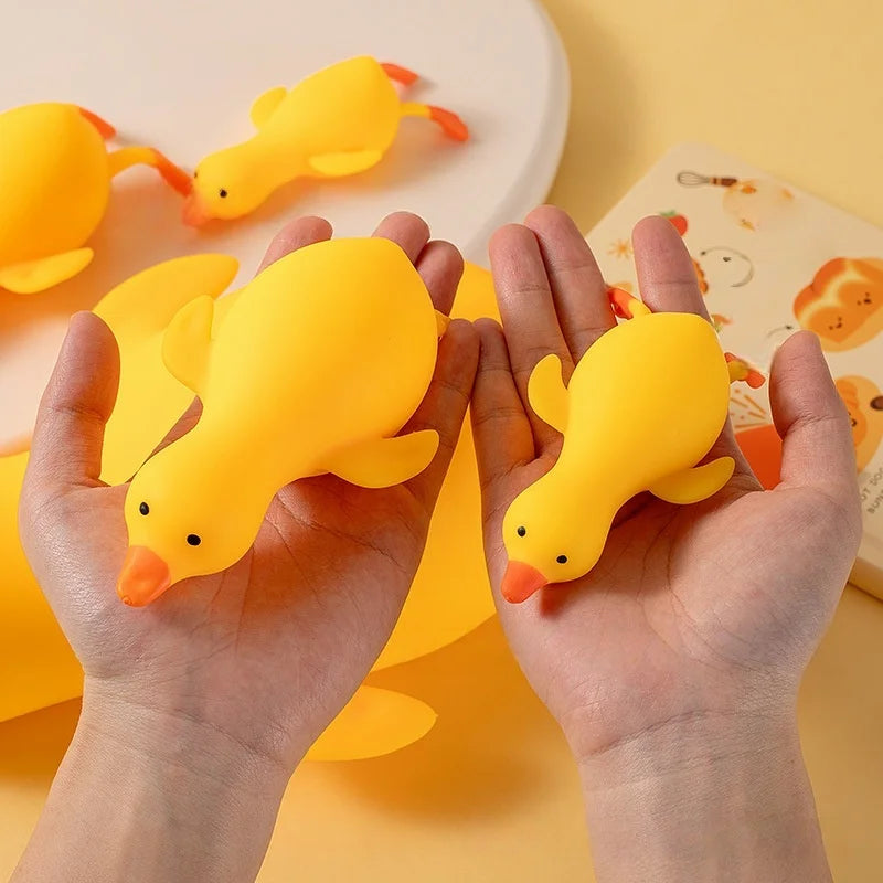 Two hands hold bright yellow squishy duck stress balls against a light background.