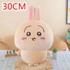 A soft pink Chiikawa plush doll resembling a rabbit with large eyes sitting on a woven mat.