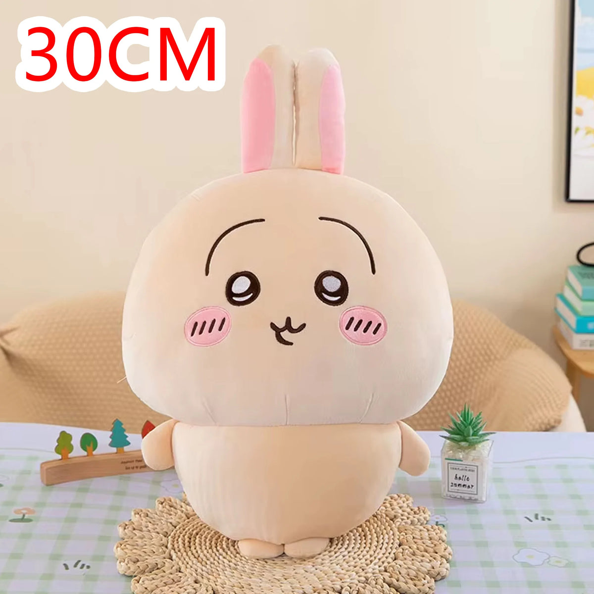 A soft pink Chiikawa plush doll resembling a rabbit with large eyes sitting on a woven mat.