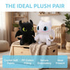 A black dragon plush and a white cartoon animal plush pair displayed on a wooden box with a knitted blanket.