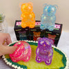 A purple glitter bear squishy toy is displayed on a green cake, alongside other squishy toys.