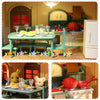 A miniature dollhouse set featuring a kitchen area with green cabinets, red pots, and wooden furniture.