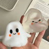 A hand holds a white squishy toy shaped like a ghost, with an orange facial expression, next to a translucent version.