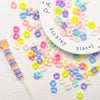 A collection of colorful pastel wavy acrylic beads in various shades are scattered on a white surface next to a white plate.
