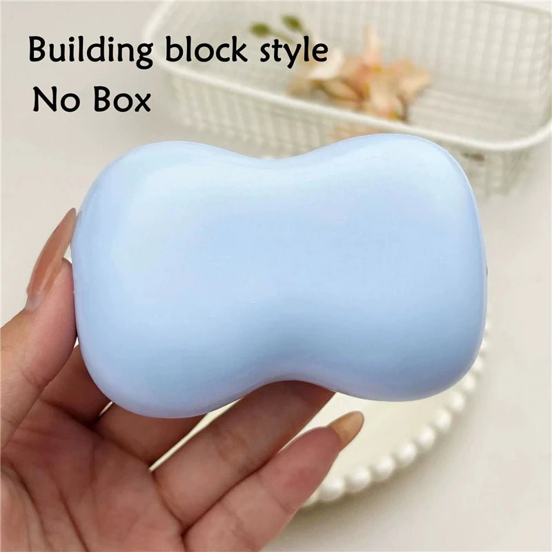 A hand holds a light blue building block style squishy fidget toy against a white background.