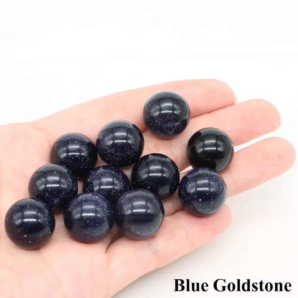 A hand holds several dark blue goldstone crystal spheres.