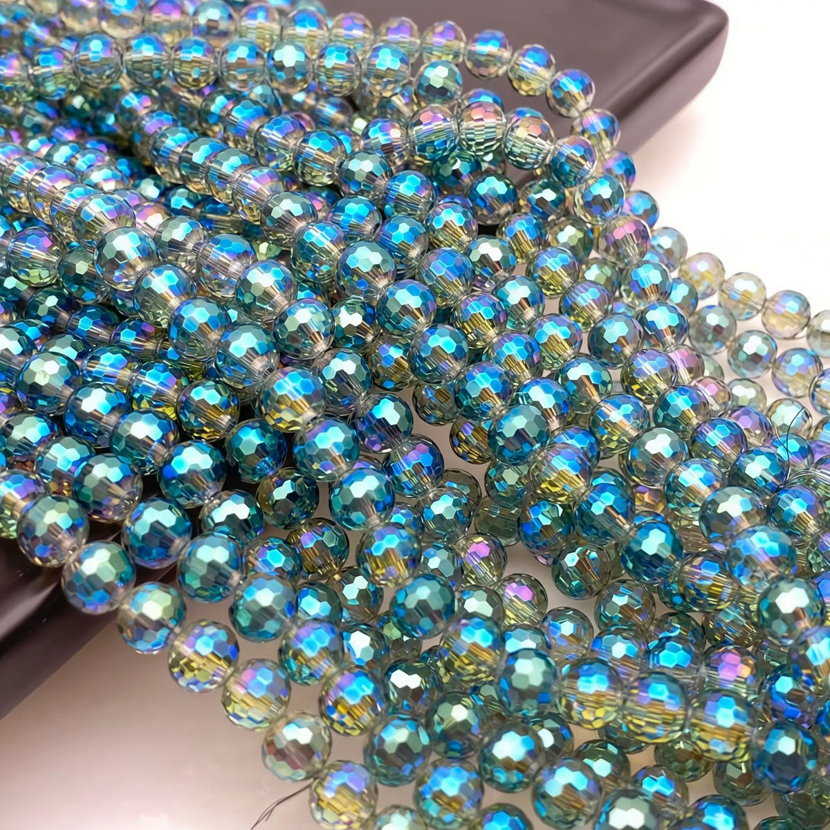 A close-up of a strand of iridescent blue and green crystal beads with an AB coating.