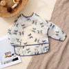 A white waterproof long sleeve feeding bib with a light floral pattern is displayed on a beige knitted fabric.