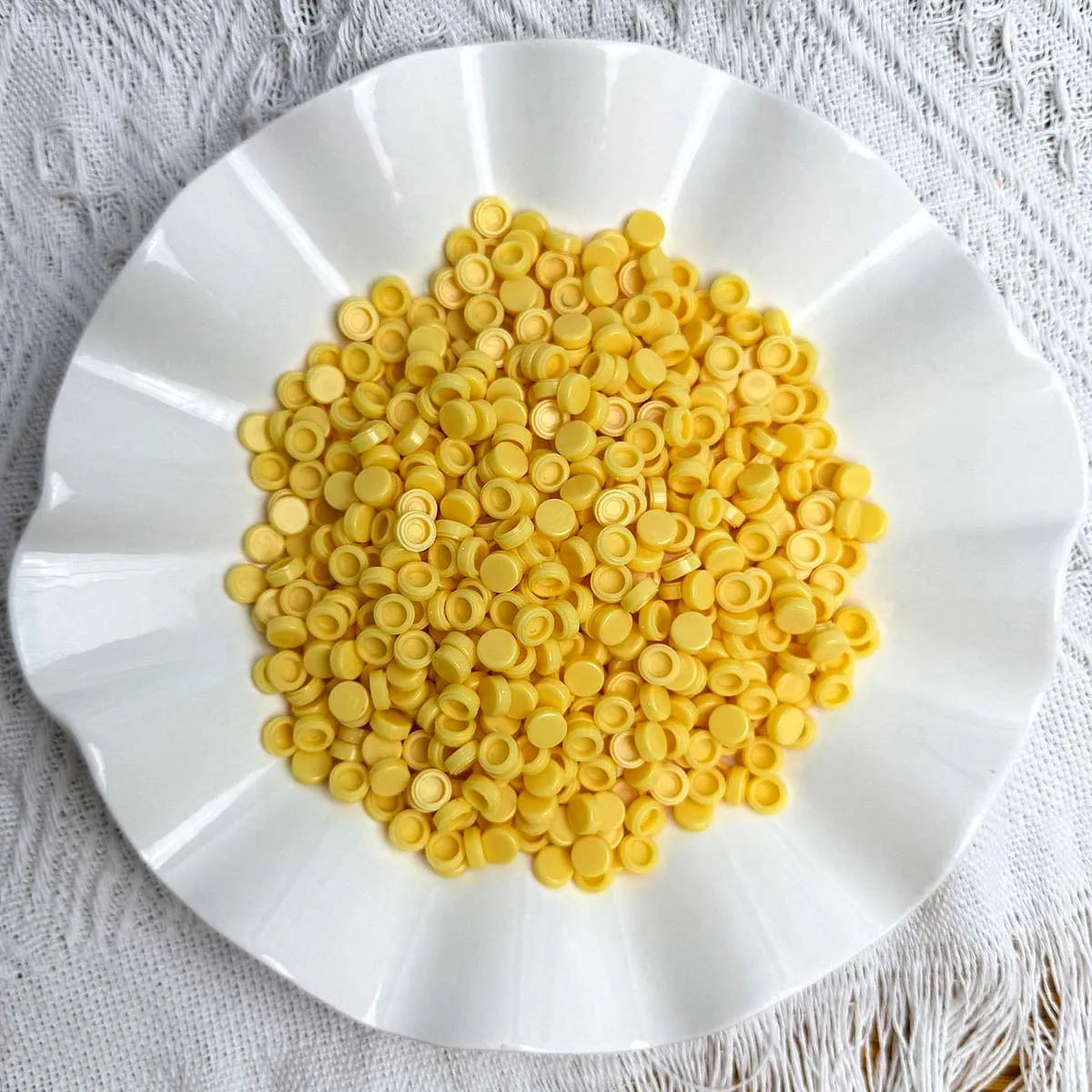 A white plate filled with yellow plastic bead filler for DIY squishy toys and crafts