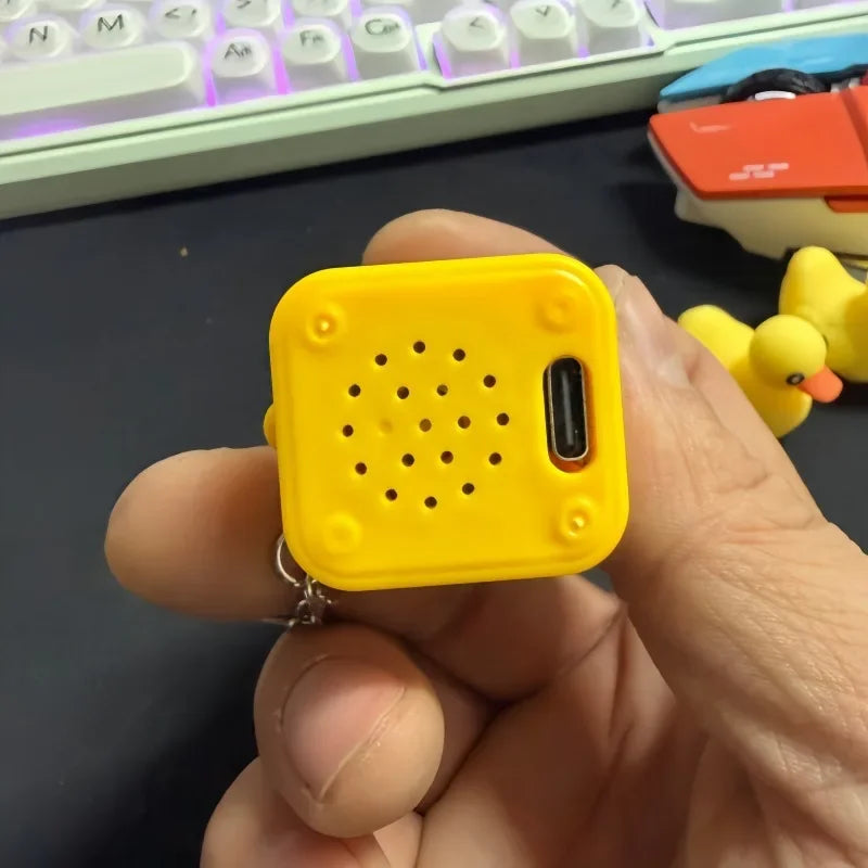 A hand holds a yellow fidget clicker keychain with a black button and a small metal ring.