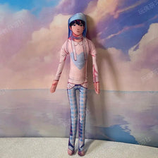 A poseable plush doll figure of a female character with blue hair and pink clothing standing against a cloudy sky background.