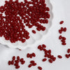 A pile of bright red oval glass rice grain beads for jewelry making on a white surface.