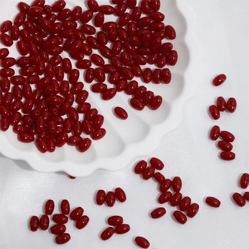 A pile of bright red oval glass rice grain beads for jewelry making on a white surface.