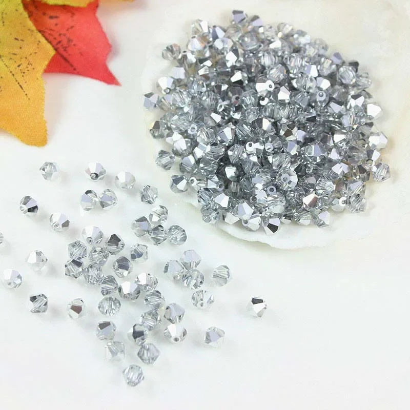 A pile of silver faceted crystal beads and loose clear crystal beads on a white surface.