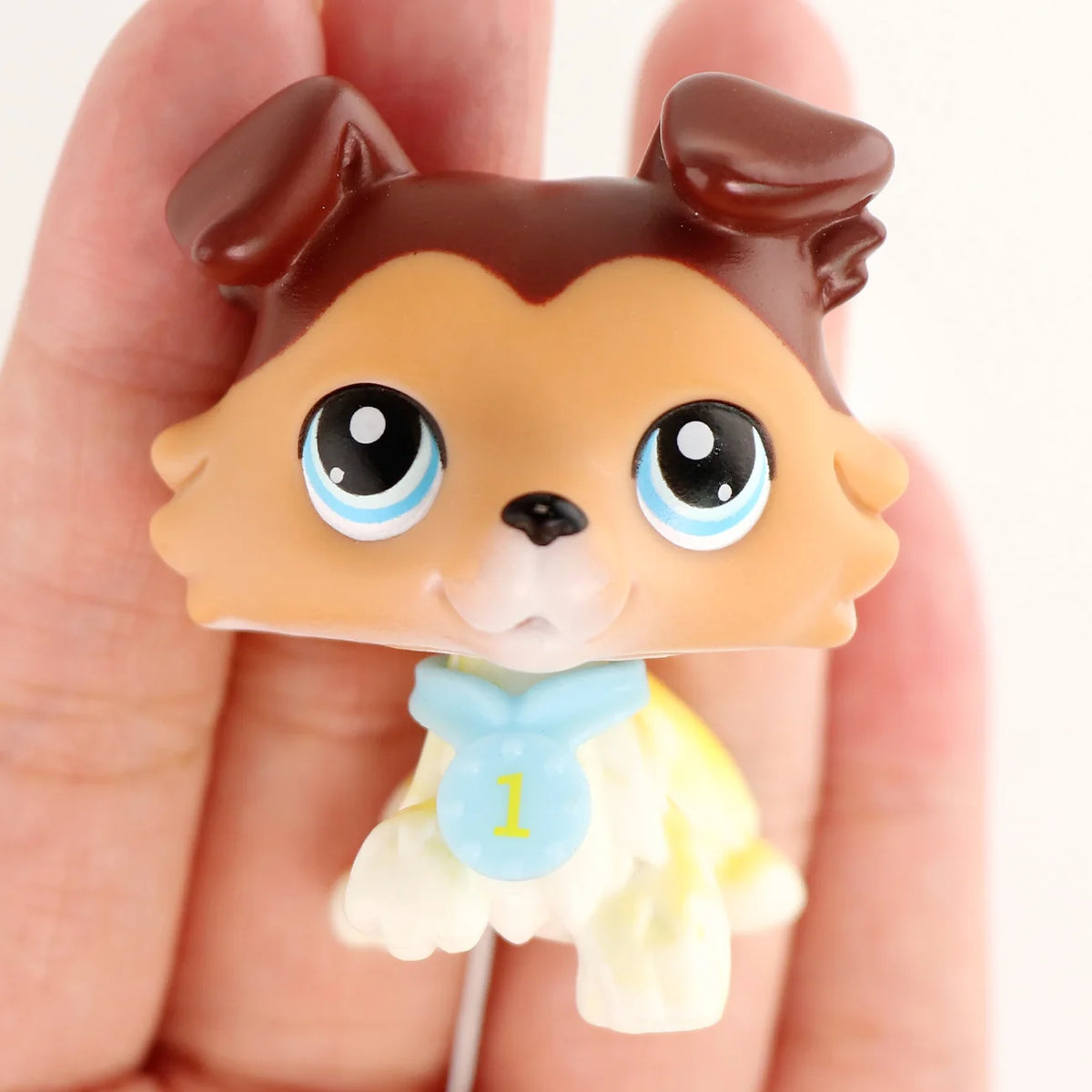 A small, brown and tan miniature pet animal figure with large blue eyes and a light yellow accessory.