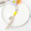 A soft bunny plush keychain with a yellow bow charm is displayed on a white plate.