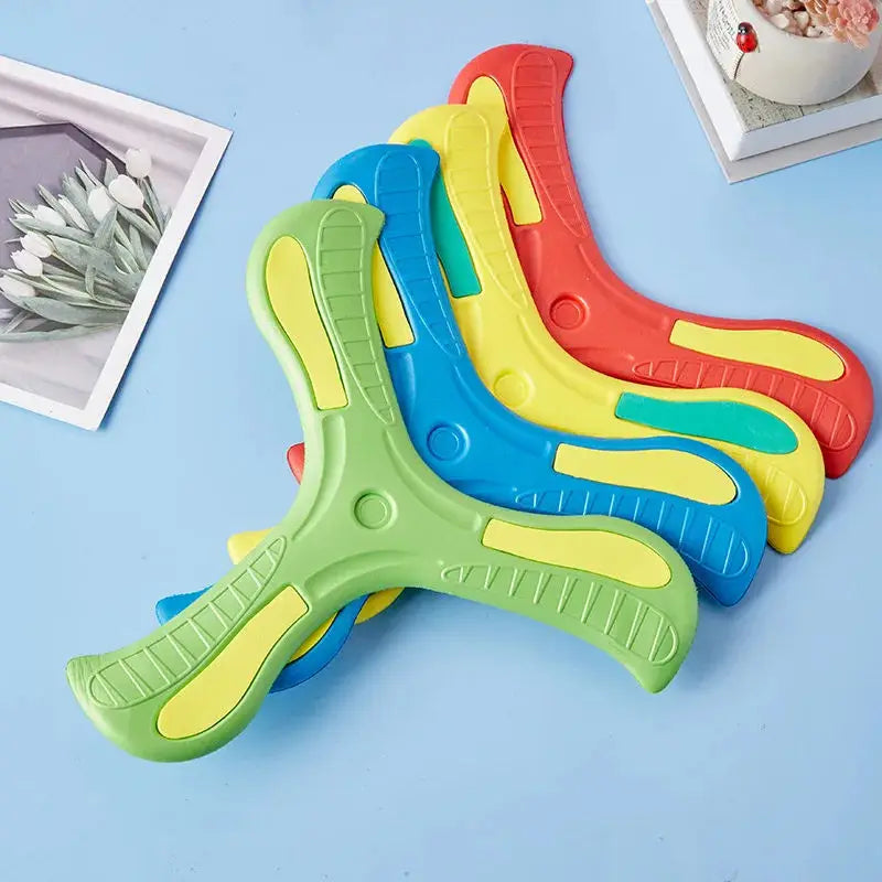 A collection of colorful soft foam boomerang flying discs in green, yellow, blue, and red are displayed on a light blue surfa