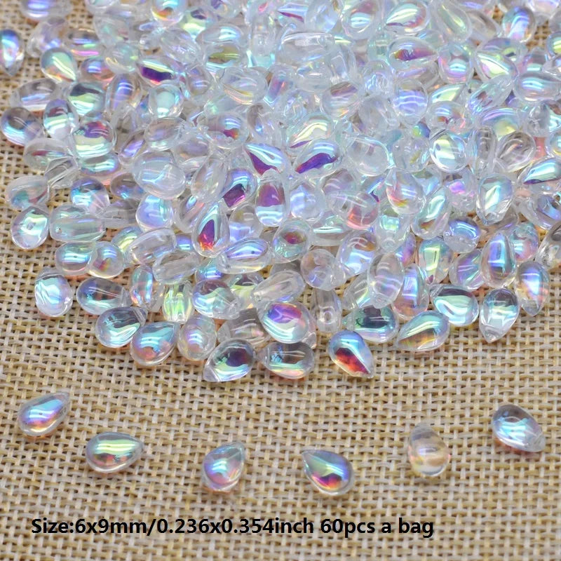 Clear iridescent water drop glass beads scattered on a beige surface