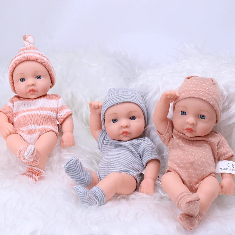 A set of realistic soft vinyl reborn baby dolls dressed in striped clothing and knitted hats, lying on white fluffy material.