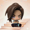 A blind box figure of a character with dark brown hair and intense expression sitting on a stack of books.