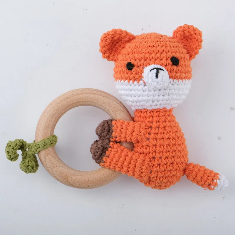 An orange crocheted bear toy attached to a wooden ring, used as a baby rattle and teether.