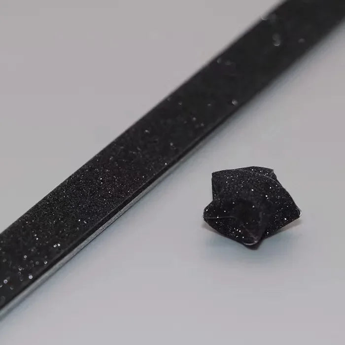 A close-up view of black glitter origami star paper strips lying on a white surface.
