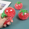 A hand holds a translucent red squishy tomato stress relief fidget toy with green leaves.
